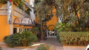 Entrada de hotel con un corredor cubierto, rodeada de exuberante follaje y palmeras.