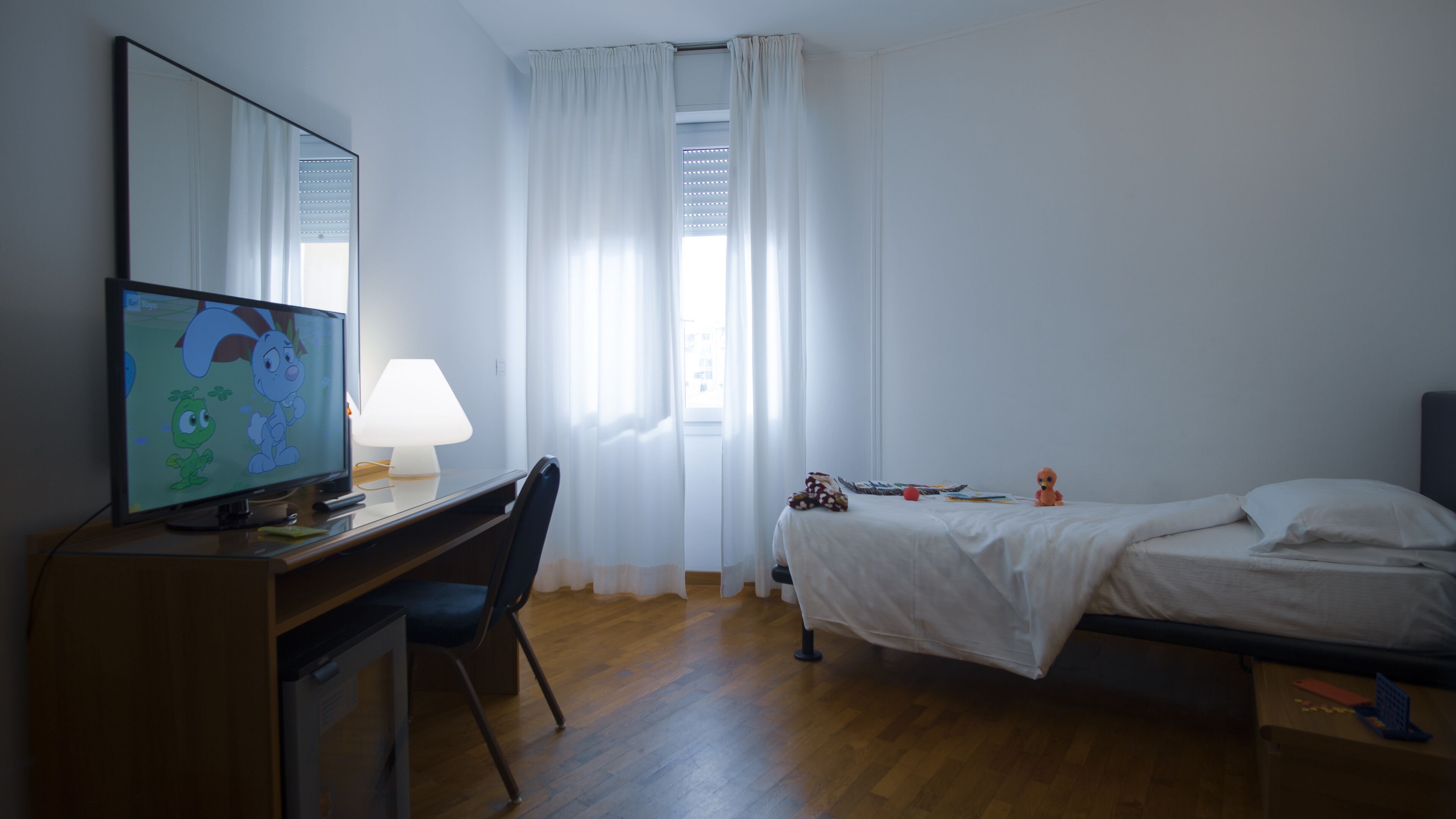 Una habitación de hotel con escritorio de madera, televisor, cama y ventana con cortinas.