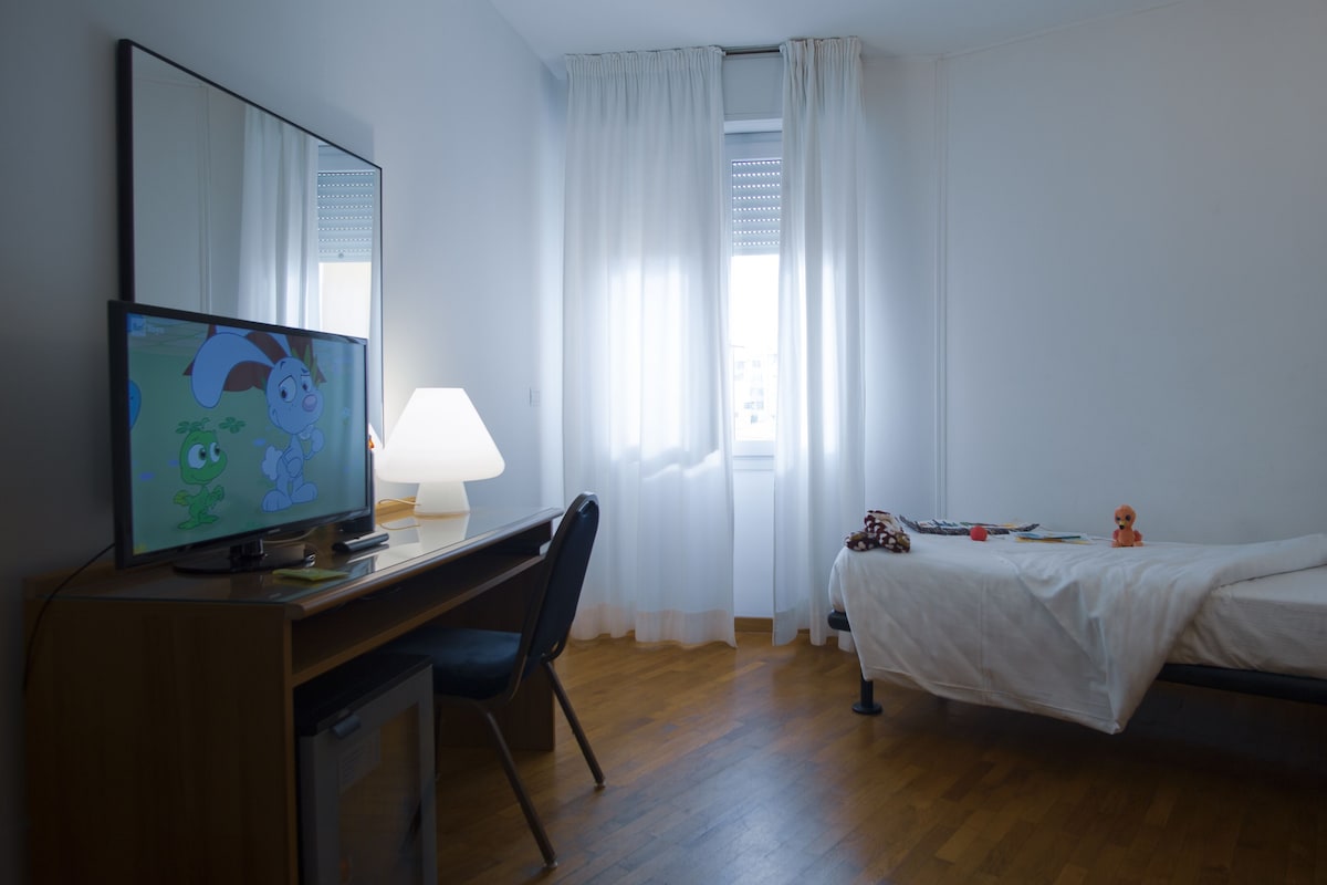A hotel room with a wooden desk, a television, a bed, and a window with curtains.