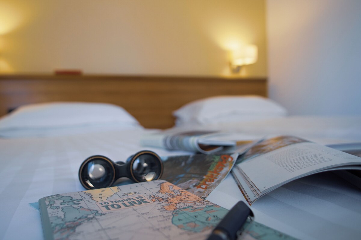 A bed with a map, a pen, and a pair of glasses on it.