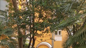 An outdoor patio area with brick flooring, green metal chairs, and tables. There is a yellow building with a curved entrance and a door. - Hotel Mistral 2 (Oristano)
