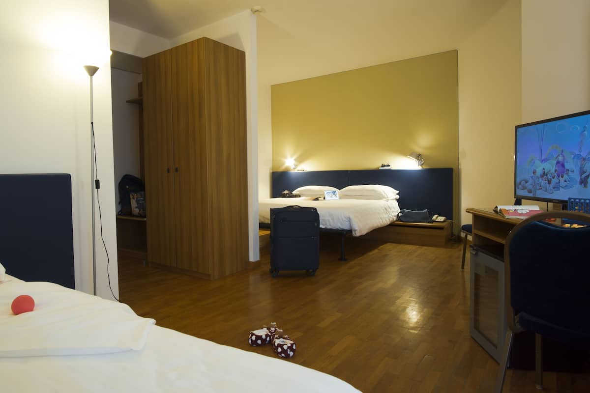 A hotel room with a bed, a desk with a computer, a television, and a wardrobe.