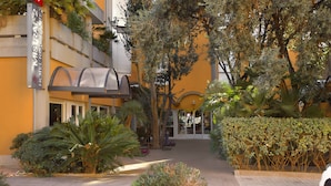 A hotel entrance with a covered walkway, surrounded by lush greenery and palm trees. - Hotel Mistral 2 (Oristano)