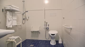 Un bagno moderno con un water bianco, una doccia con soffione manuale, un portascopino con asciugamani piegati e un pavimento in piastrelle blu.