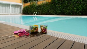 A pool area with a wooden deck, poolside chairs, and bags of snacks. - Hotel Mistral 2 (Oristano)