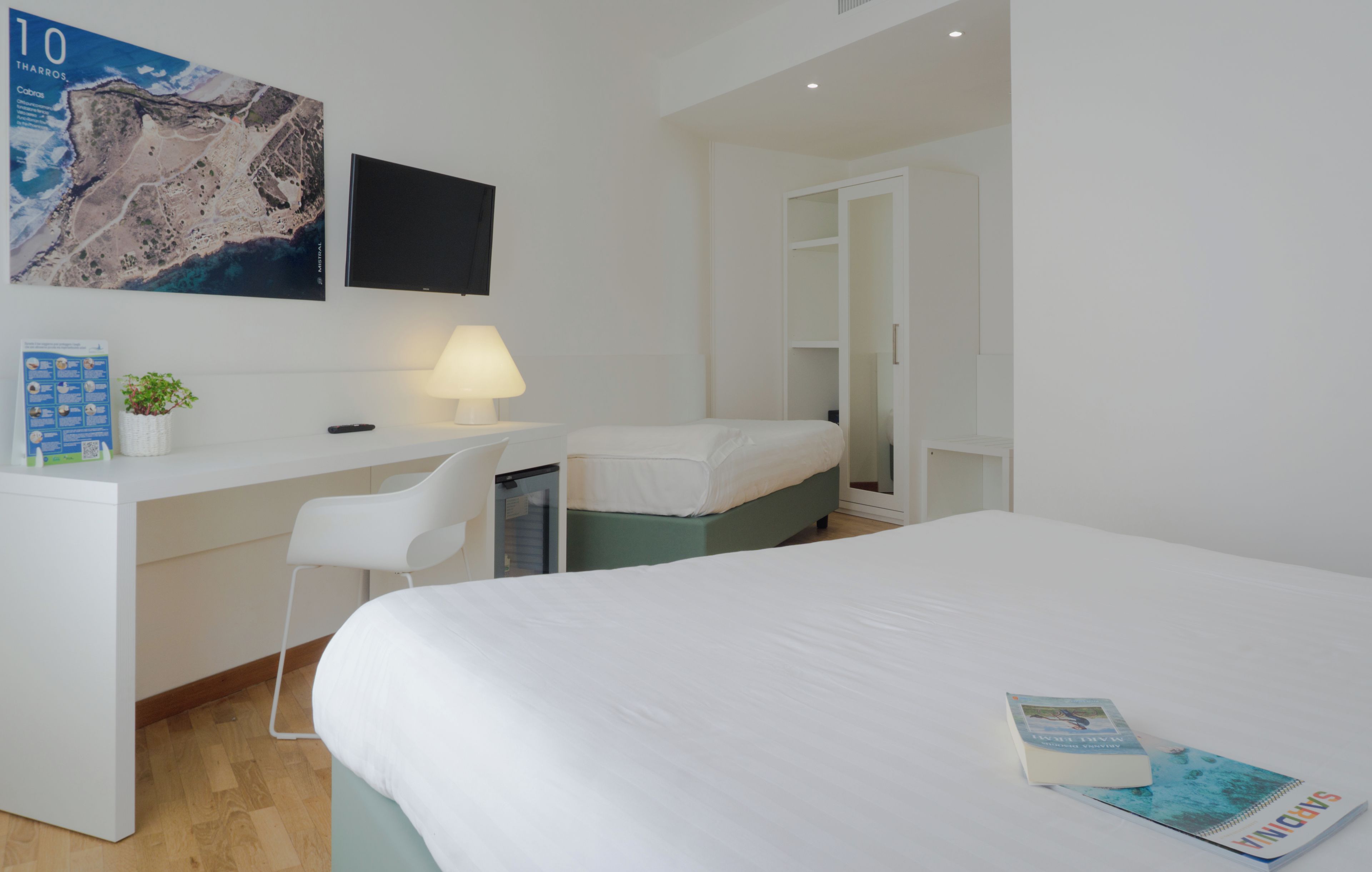 Habitación de hotel con cama, escritorio, silla, televisor y armario.
