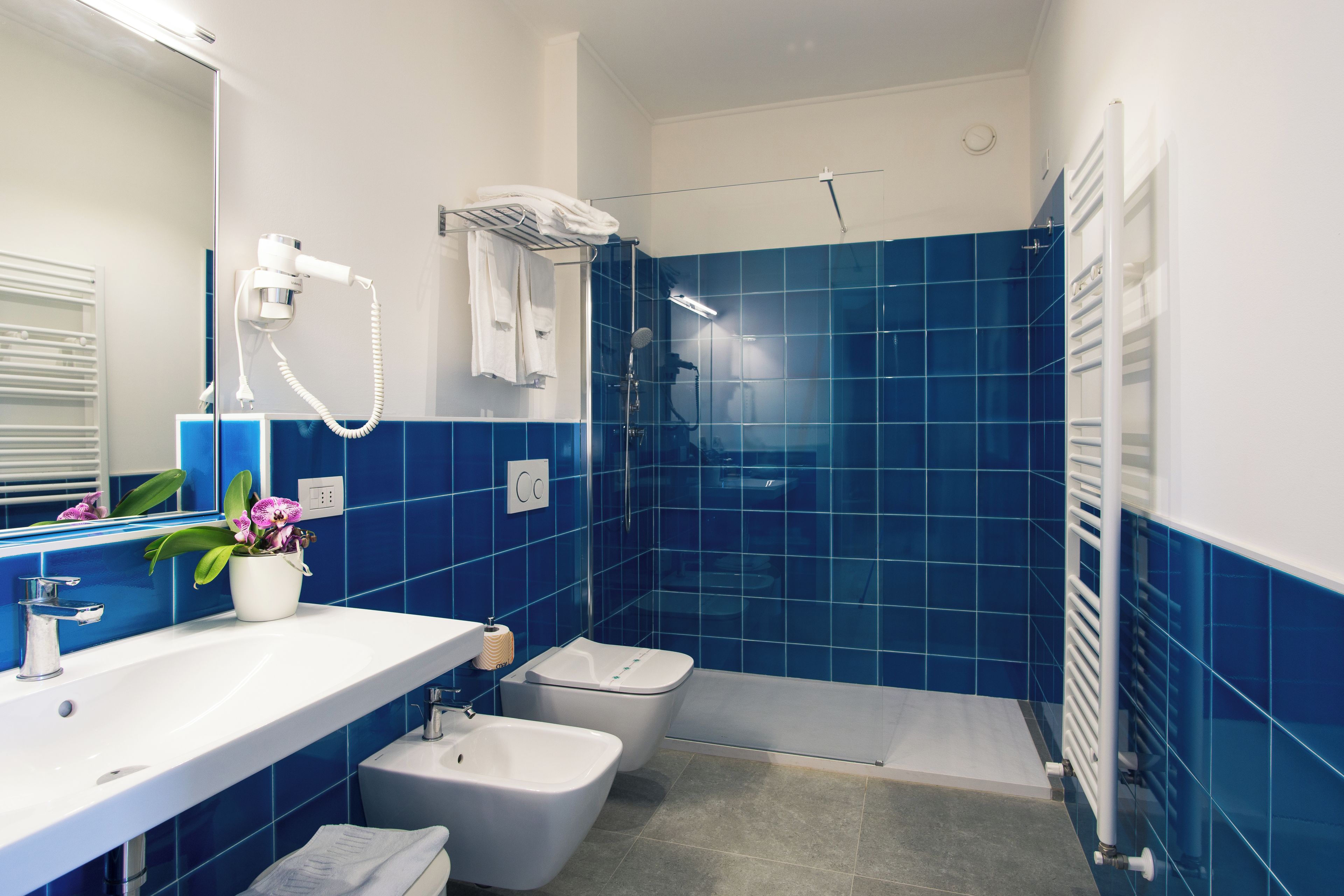 A bathroom with a white sink, a bidet, a shower with a glass door, and a towel rack.