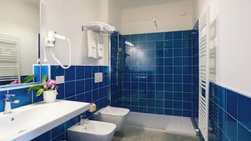 A bathroom with a white sink, a bidet, a shower with a glass door, and a towel rack.