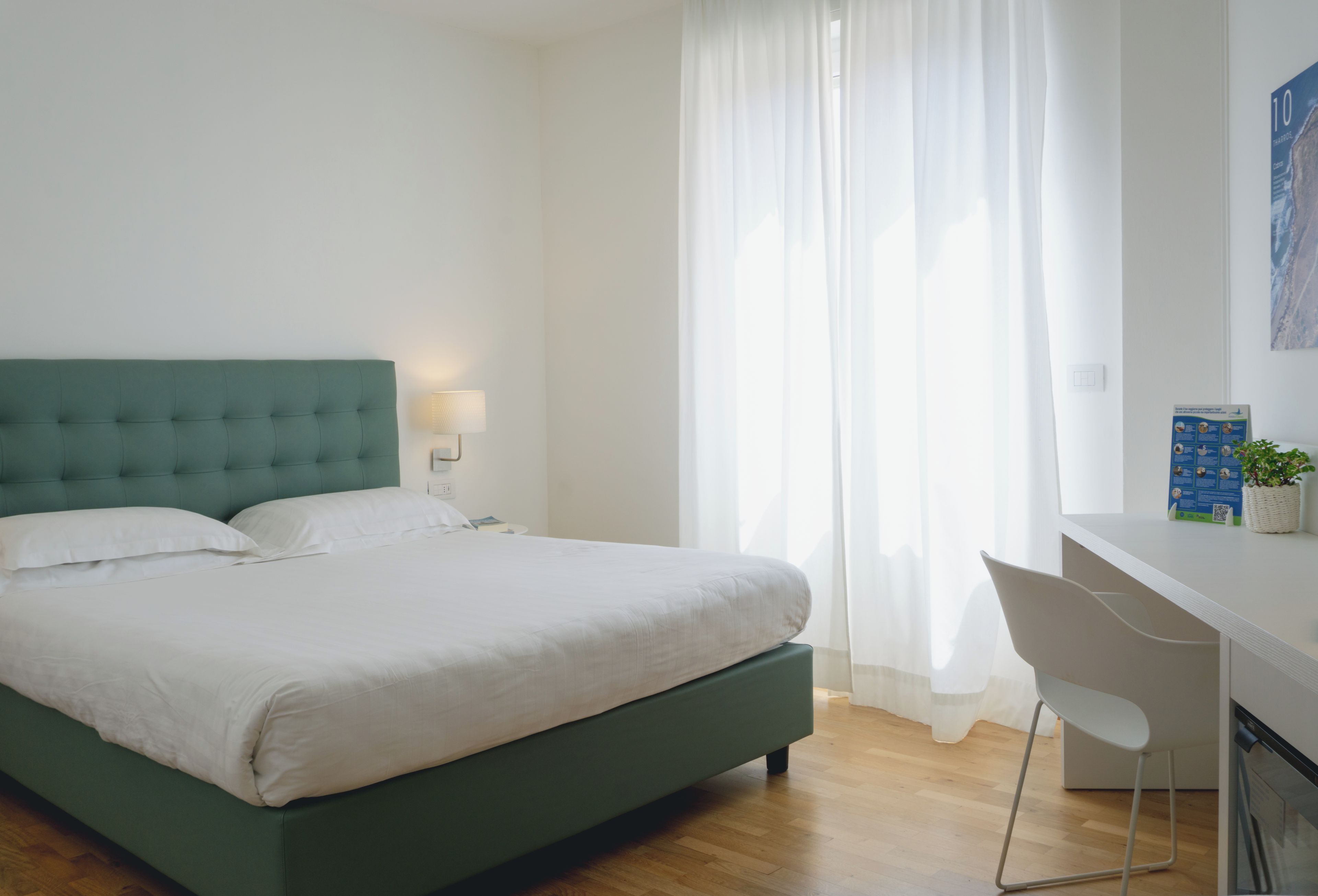 Ein Schlafzimmer mit einem Bett, einem Schreibtisch, einem Stuhl und einem Fenster mit Vorhängen.