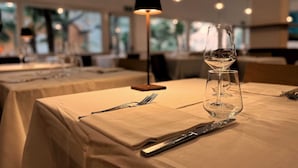 Una mesa de comedor preparada con una copa de vino, cubiertos y una lámpara.