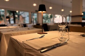 A dining table set with a wine glass, cutlery, and a lamp. - Hotel Mistral 2 (Oristano)