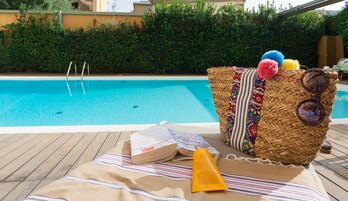 Zona junto a la piscina con una cesta de mimbre que contiene un libro, protector solar y gafas de sol.