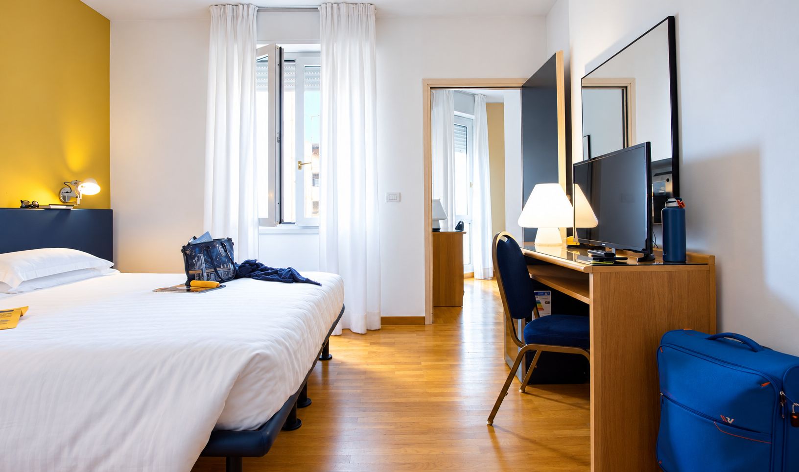 Habitación de hotel con cama, escritorio, silla y maleta.