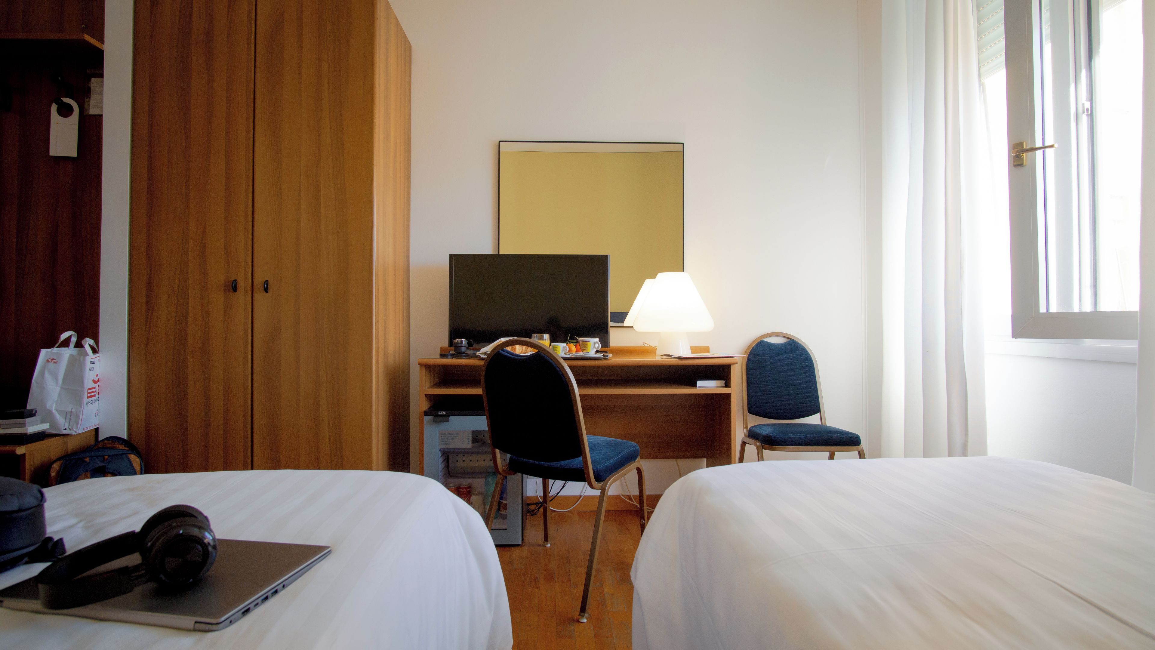 Een hotelkamer met twee bedden, een bureau met een computer, een stoel, een lamp en een televisie.