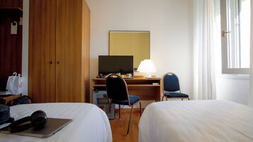 Een hotelkamer met twee bedden, een bureau met een computer, een stoel, een lamp en een televisie.