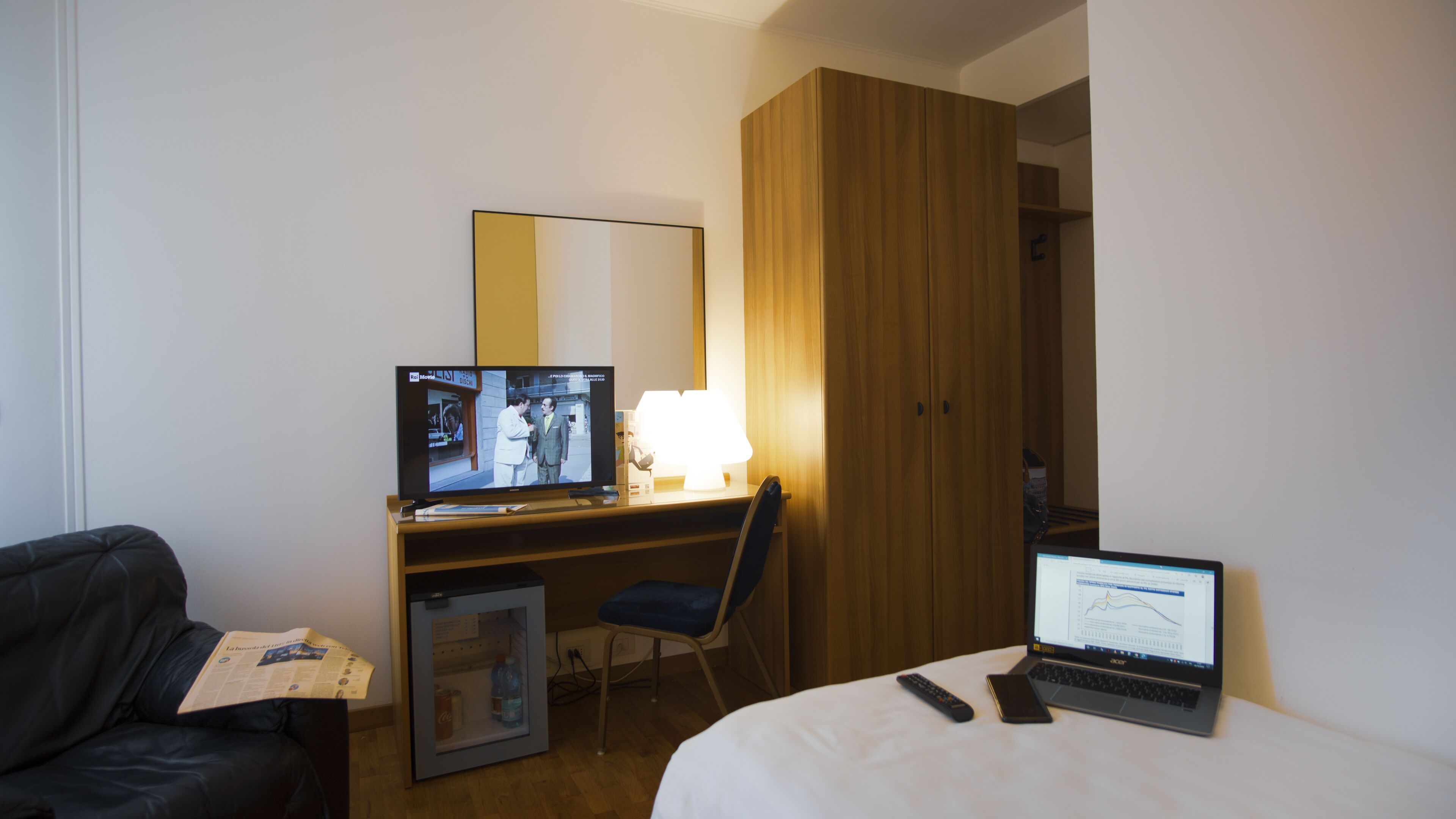 Una habitación de hotel con cama, escritorio con computadora, silla, televisor y armario.