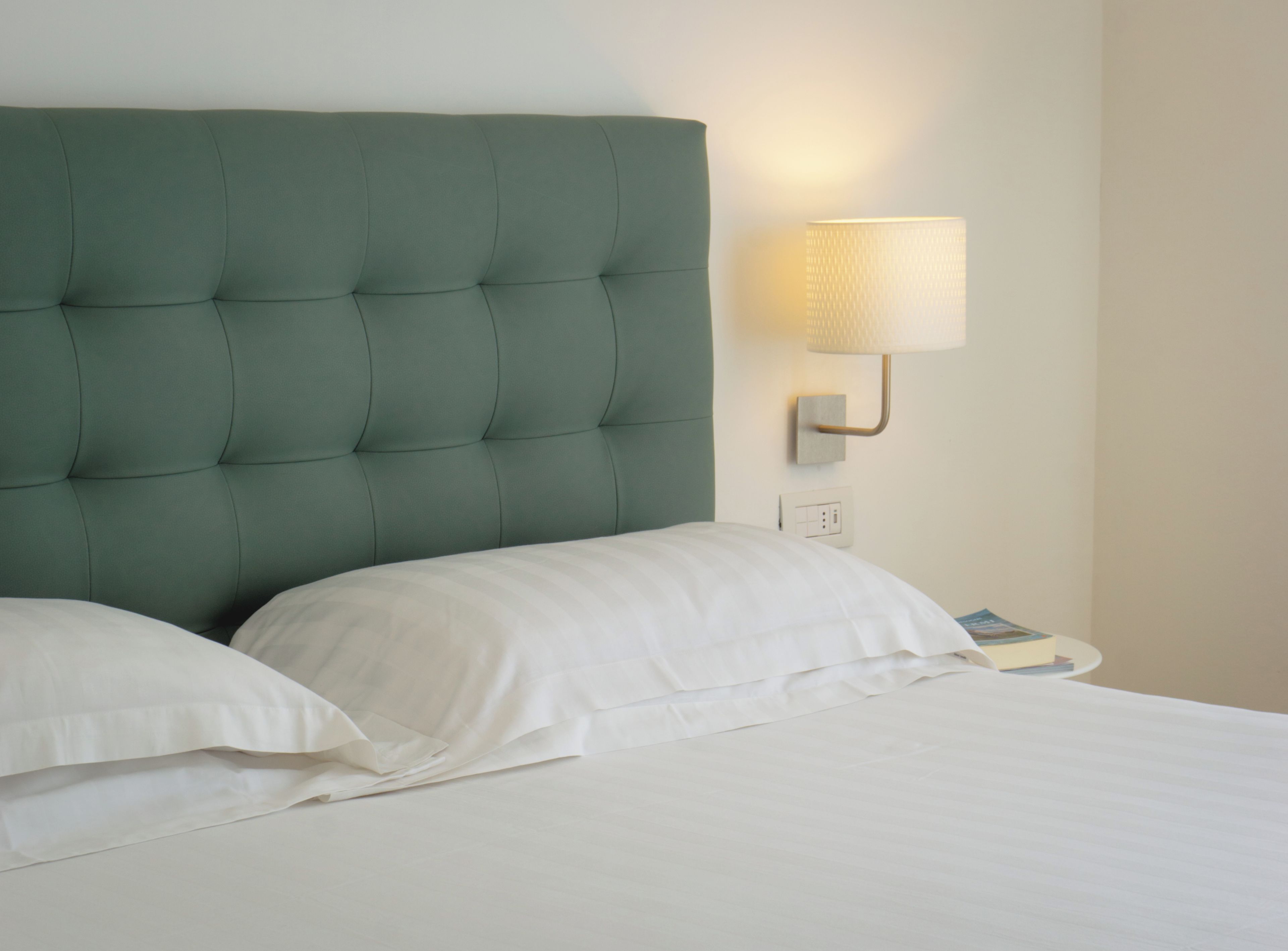 Een bed met een gestoffeerd hoofdeinde, een bedlampje en een boek op het nachtkastje.