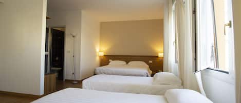 A hotel room with two single beds, a bedside table, a lamp, and a window with curtains.