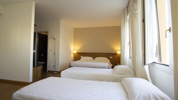 Habitación de hotel con dos camas individuales, una mesita de noche, una lámpara y una ventana con cortinas.