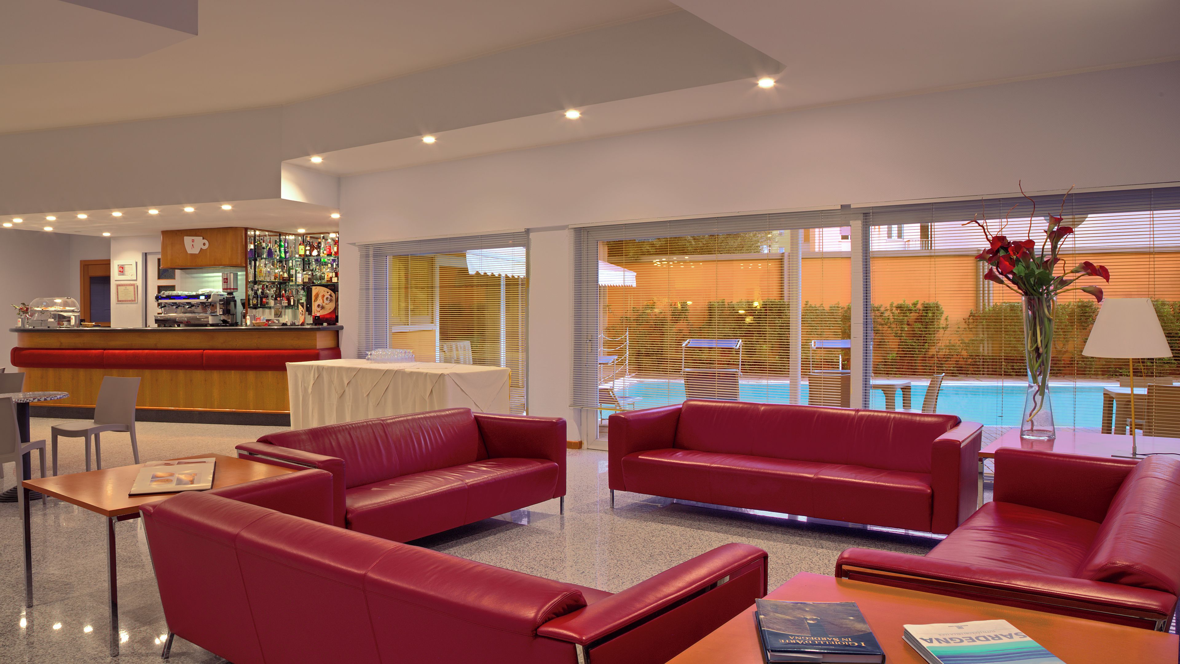 Un moderno vestíbulo de hotel con sofás de cuero rojo, una zona de bar y vistas a la piscina.