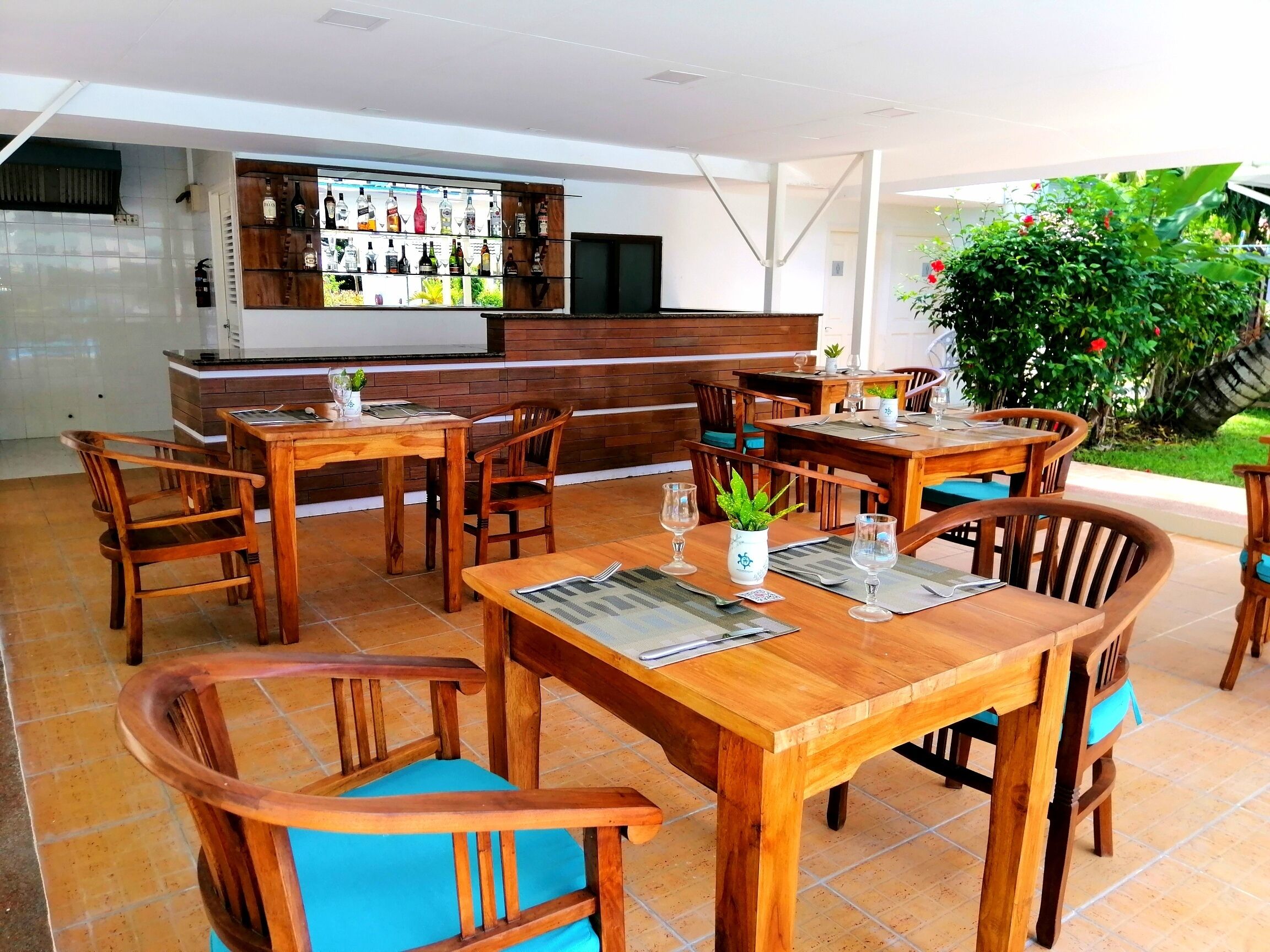 Ein Restaurant mit Holztischen und -stühlen, einer Bar mit verschiedenen Flaschen und Blick ins Grüne.