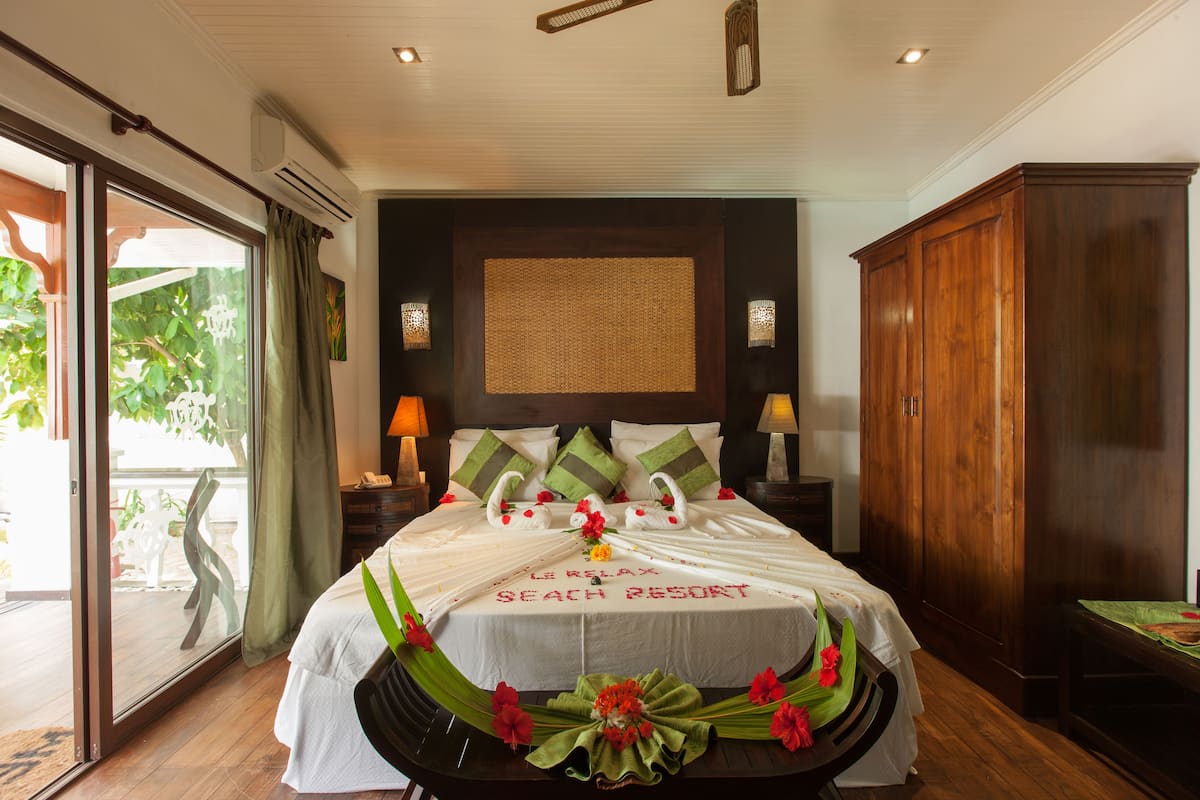 Quarto bem iluminado com uma cama grande, um guarda-roupa de madeira e vista para o verde através de uma porta deslizante.