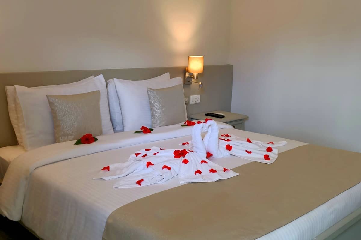 Cama bem arrumada com lençóis brancos e pétalas de rosa vermelhas, duas luminárias de cabeceira e uma cabeceira moderna.