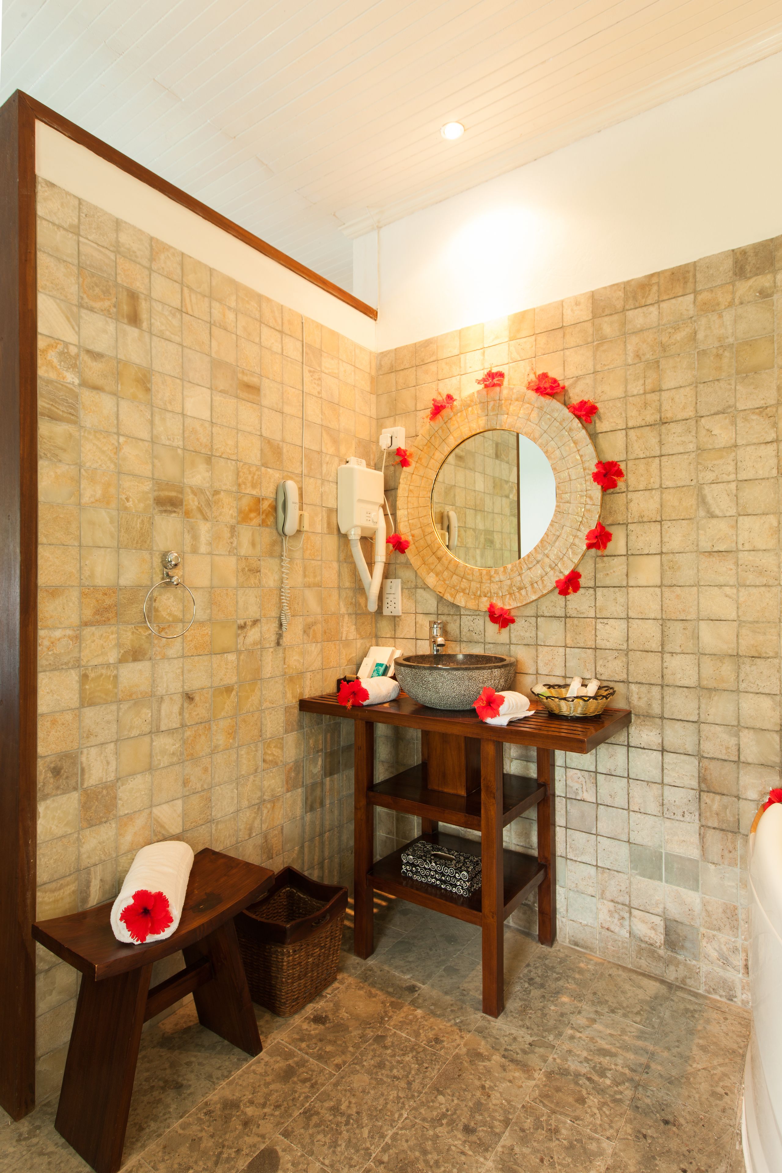 Een badkamer met een betegelde muur, een houten wastafelmeubel, een ronde spiegel, een wastafel, een handdoek en een mand.