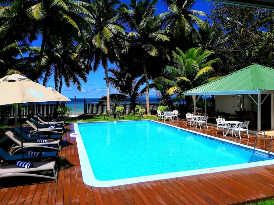 Piscina retangular com um deque de madeira, cercada por espreguiçadeiras e guarda-sóis.