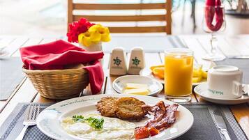Un desayuno con un plato de huevos, tocino, patatas ralladas y tostadas, un vaso de zumo de naranja y una taza de café.