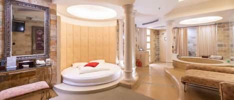A spacious bathroom with a round bathtub, a large mirror, and a vanity with a sink.