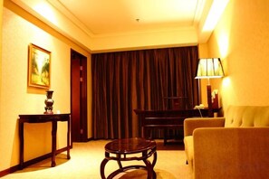 A hotel room with a sofa, a small round table, a lamp, and a painting on the wall. - Mascot Hotel (Zhongshan)