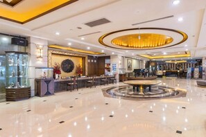 A spacious lobby with a central circular seating area, a reception desk, and a display of decorative items. - Mascot Hotel (Zhongshan)
