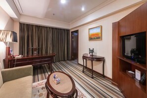 Een hotelkamer met een bank, een klein rond tafeltje, een televisie, een schilderij aan de muur en een gestreept tapijt.