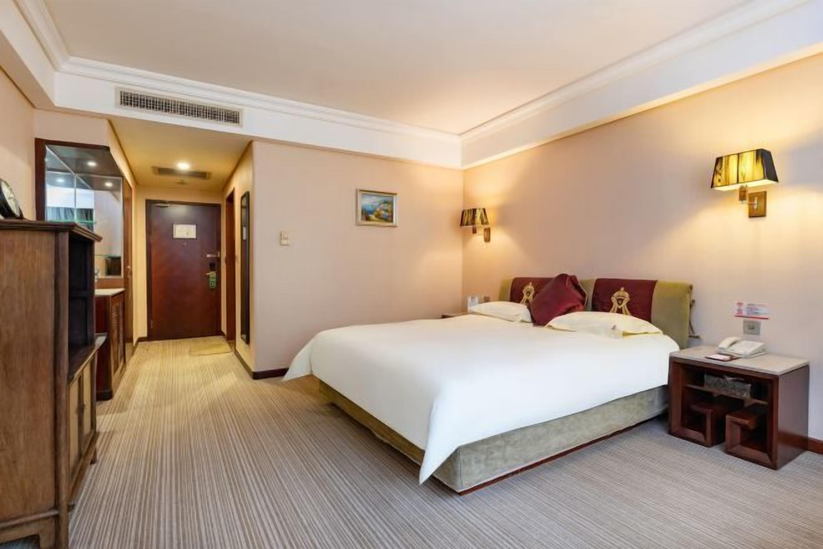 A hotel room with a large bed, a bedside table with a lamp, and a wardrobe.