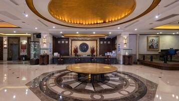 A hotel lobby with a central round table, reception desk, and a decorative wall.