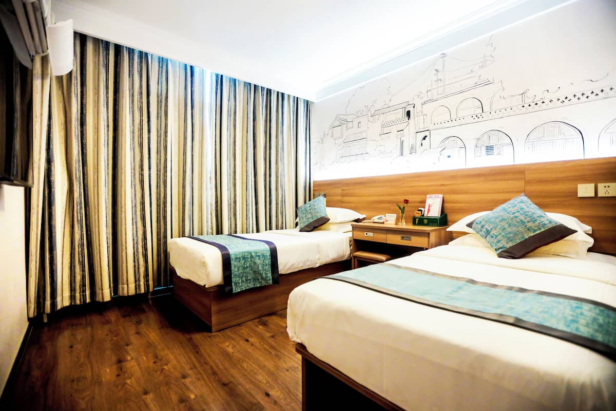 Habitación de hotel con dos camas, suelo de madera, cortinas a rayas, una mesita de noche y un mural en la pared.