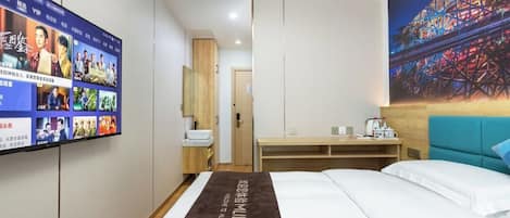 A hotel room with a bed, a desk, a TV on the wall, and a painting of a roller coaster.