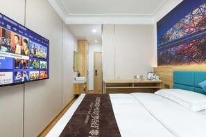 Una habitación de hotel con cama, escritorio, televisor en la pared y un cuadro de una montaña rusa.
