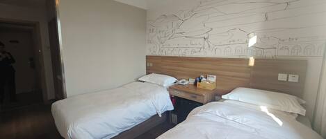 Ein Hotelzimmer mit zwei Betten, einem hölzernen Kopfteil, einem Nachttisch mit Telefon und Toilettenartikeln sowie einem Wandbild.