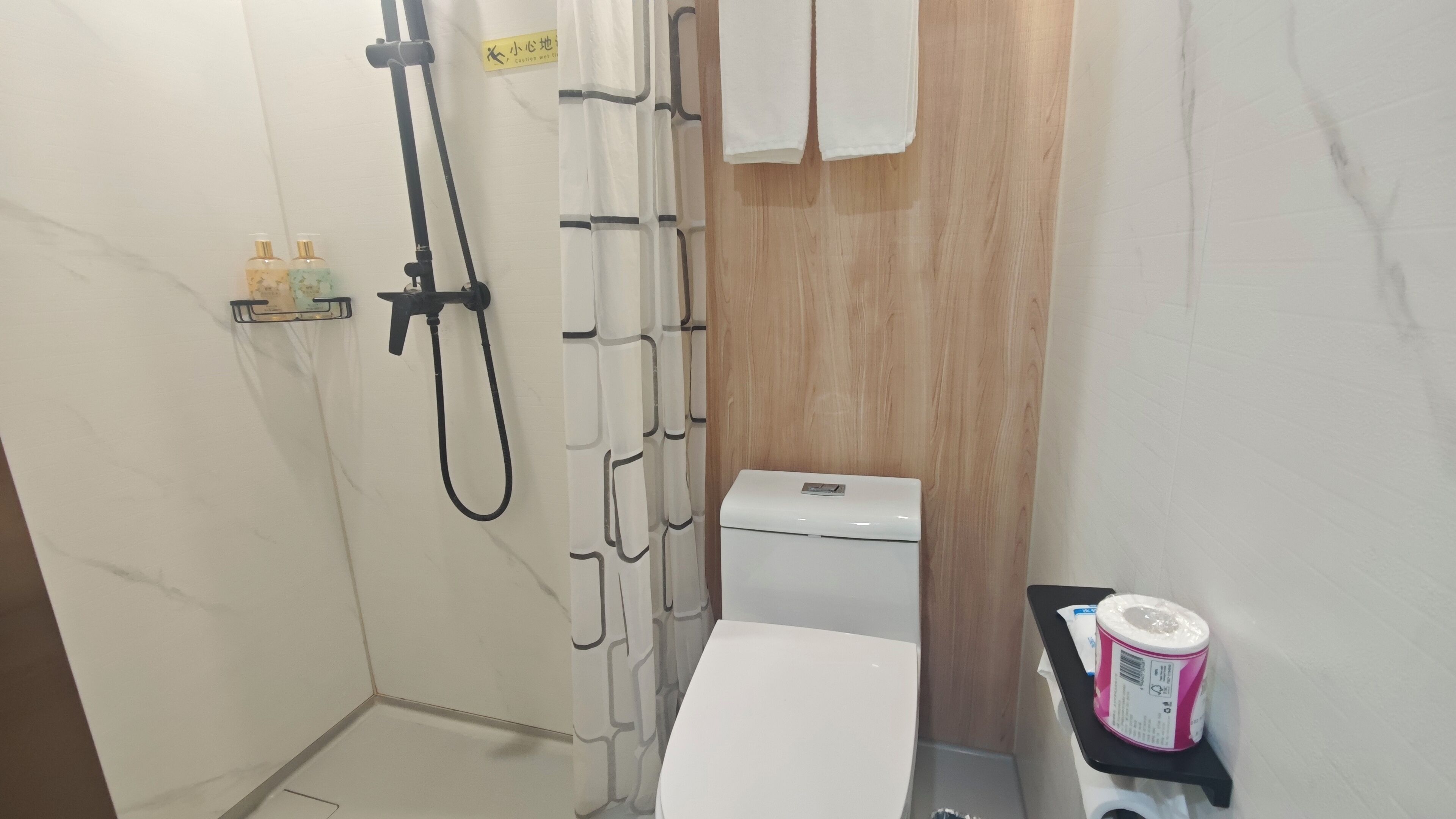 A bathroom with a shower, toilet, and a small shelf with toiletries.