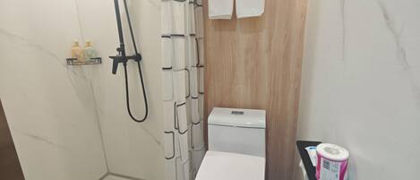 A bathroom with a shower, toilet, and a small shelf with toiletries.