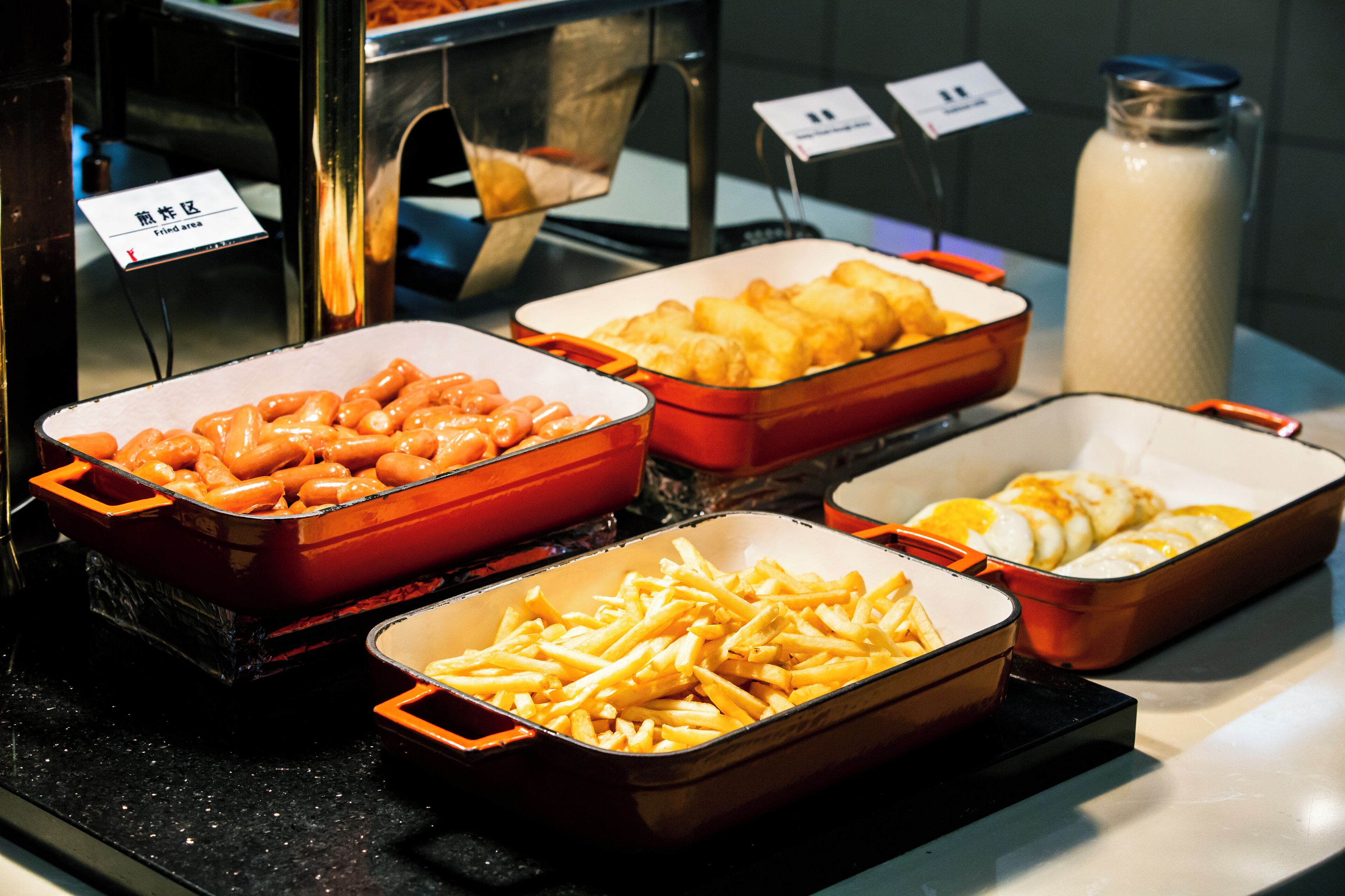 A buffet with various food items including sausages, French fries, and eggs.