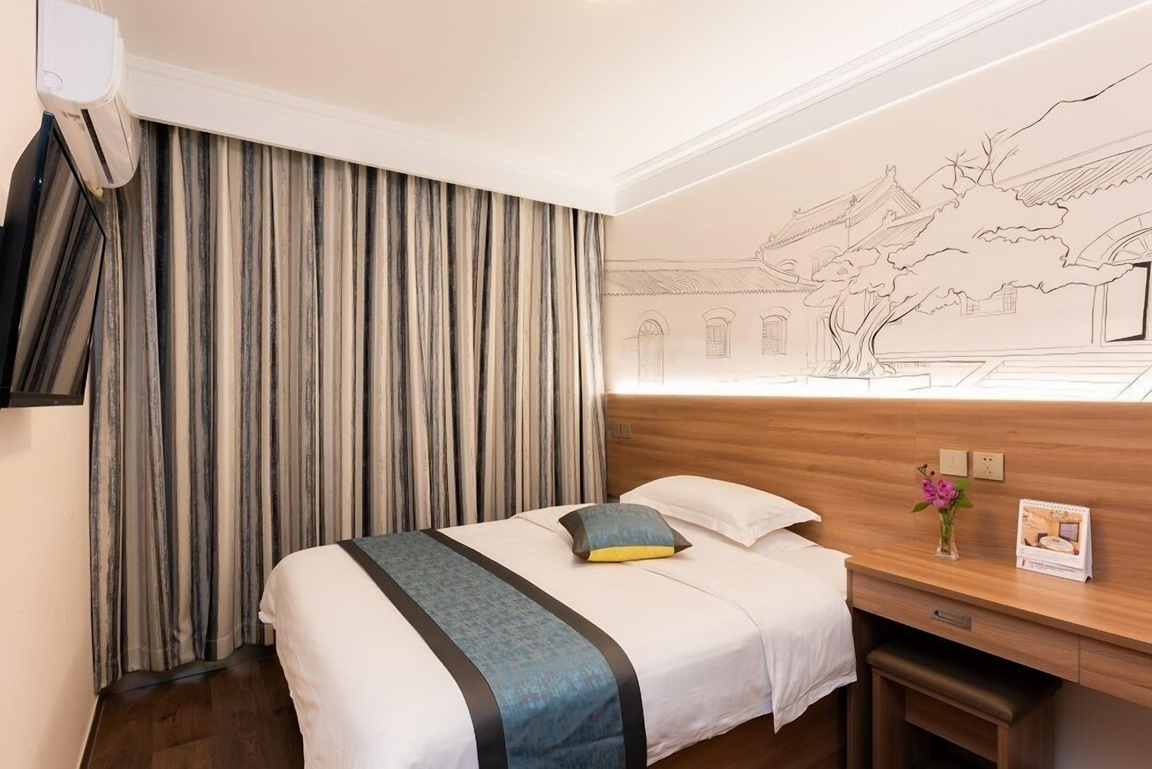A hotel room with a bed, a desk, a wall-mounted TV, and a curtain.