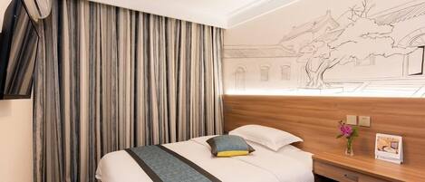Ein Hotelzimmer mit Bett, Schreibtisch, Wandfernseher und Vorhang.