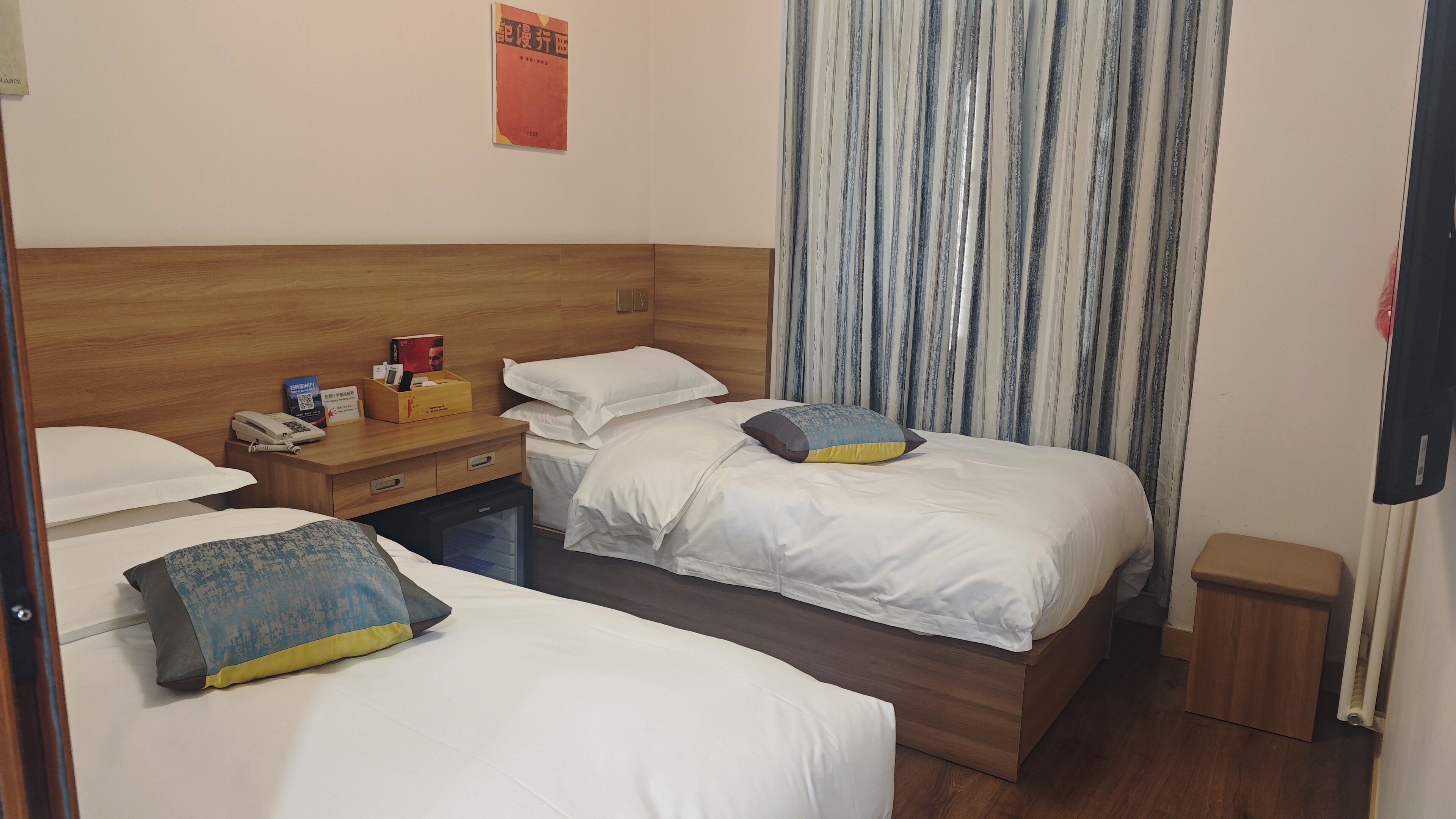A hotel room with two beds, a wooden headboard, a nightstand with a phone and a box, and a striped curtain.