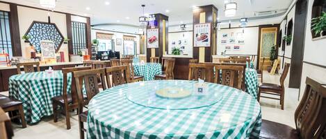 A restaurant with round tables covered in green and white checkered tablecloths, wooden chairs, and pendant lighting.