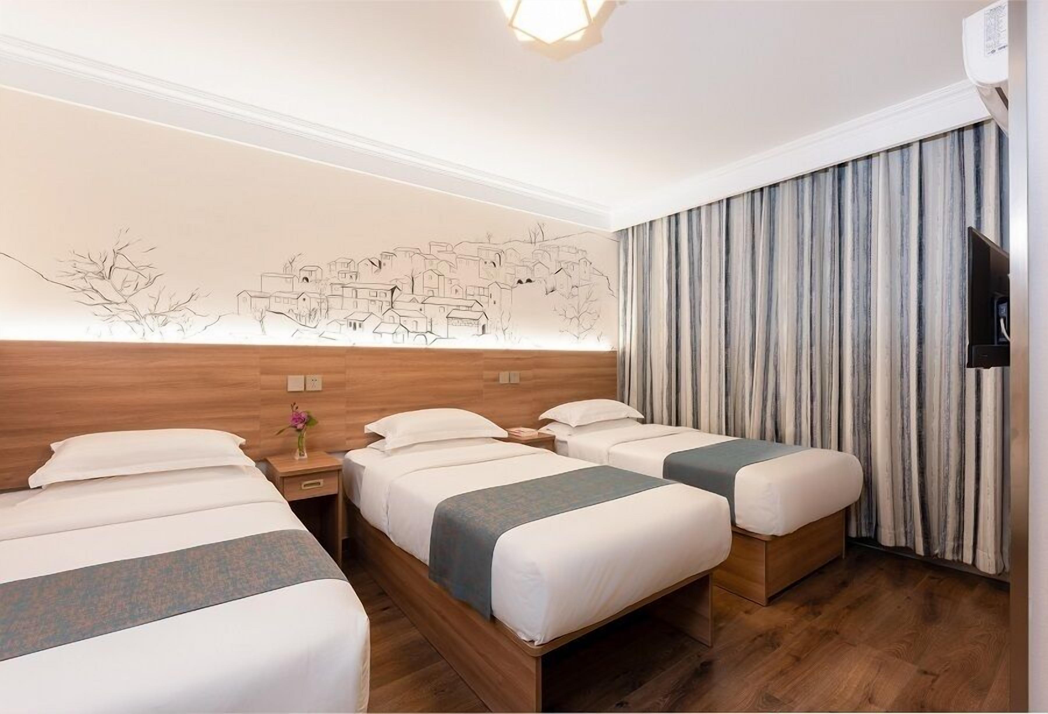 Habitación de hotel con tres camas, cabecera de madera, un mural en la pared, televisor de pantalla plana y una cortina.