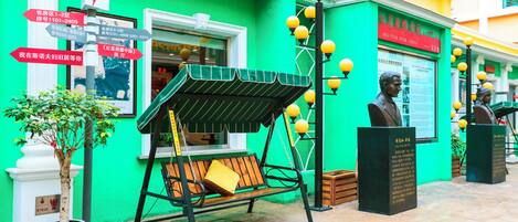 A green building with a swing bench, directional signs, and a statue.