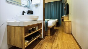 A hotel bathroom with a white sink, wooden vanity, and a mirror. There is a bed with a blue curtain in the adjacent room. - Zhongan Hotel Beijing (Beijing)